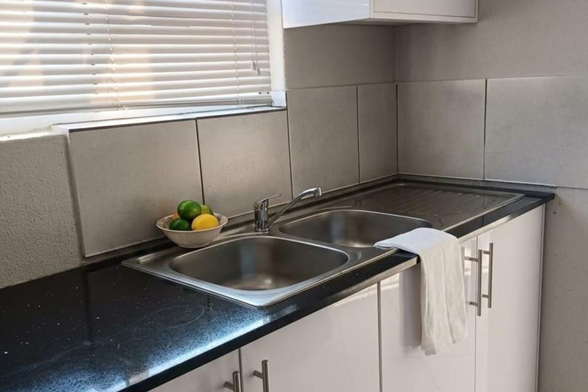 A clean and modern kitchen area featuring white high-gloss cabinetry, a black granite countertop, and a double basin stainless steel sink.