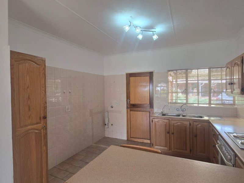 A functional kitchen featuring wooden cabinetry, laminate countertops, a double sink, and a built-in electric hob with tiled splashbacks.
