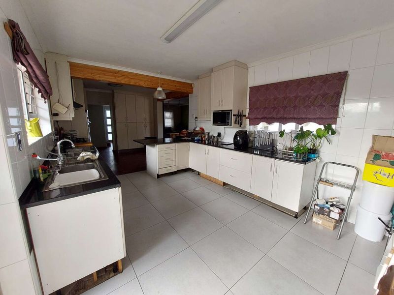 A functional kitchen featuring white cabinetry, granite countertops, tiled flooring, and an exposed timber beam, offering a practical layout with potential for cosmetic updates.