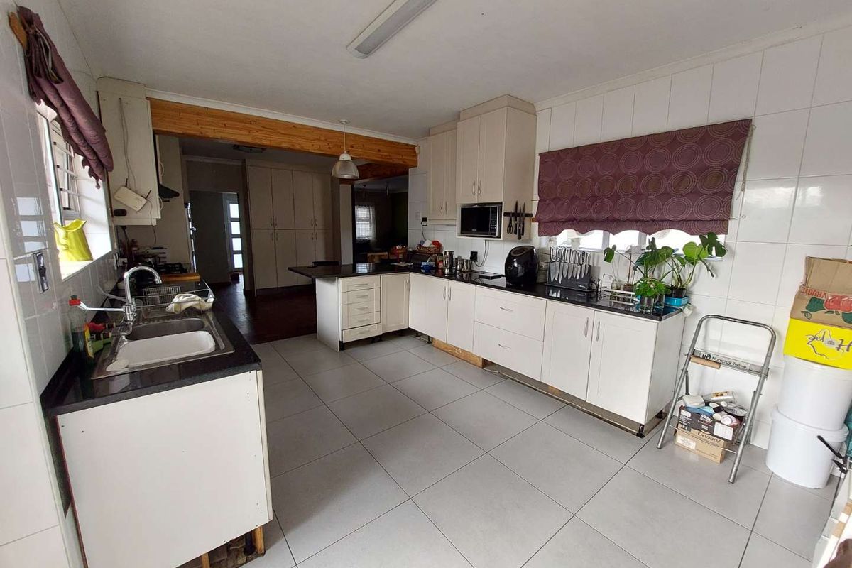 A functional kitchen featuring white cabinetry, granite countertops, tiled flooring, and an exposed timber beam, offering a practical layout with potential for cosmetic updates.