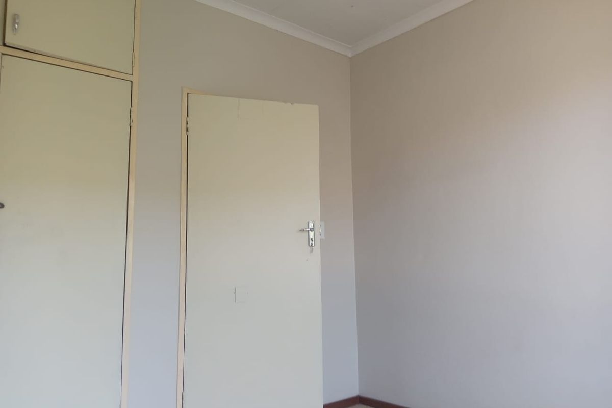 A clean, empty bedroom featuring neutral walls, tiled flooring, and built-in cupboards, offering a blank canvas for personalization.