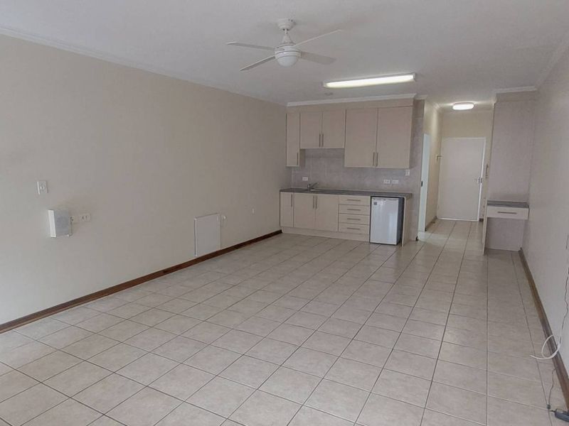An open-plan living and kitchen area featuring neutral tiled flooring, built-in cabinetry, and a ceiling fan in a retirement village setting.