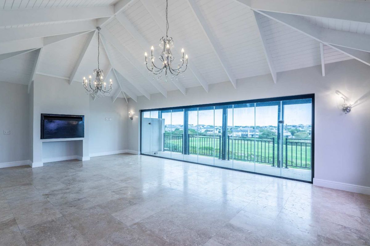 Spacious living area featuring a vaulted ceiling with exposed rafters, stone tile flooring, a built-in fireplace, and large sliding glass doors leading to a balcony.