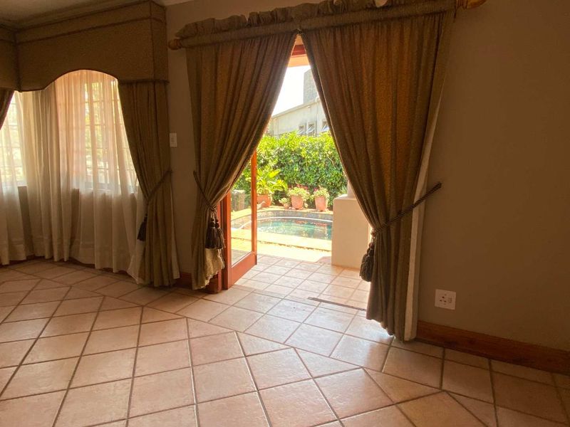 A bright living area featuring tiled flooring and an arched window, with direct access through french doors to an outdoor patio and pool area.