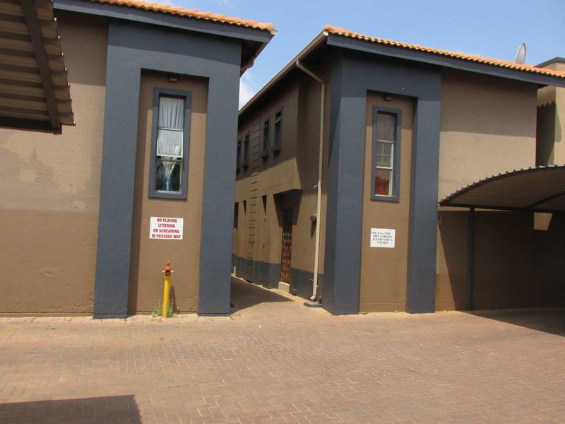 Exterior view of an apartment complex featuring paved driveway, covered parking, and a narrow walkway between building blocks.