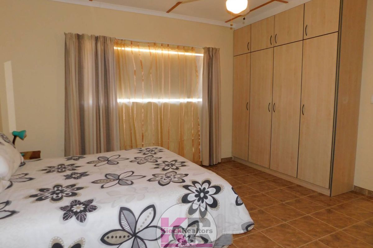 A bedroom featuring built-in wooden cupboards, tiled flooring, and a ceiling fan, providing functional storage and comfortable living space.