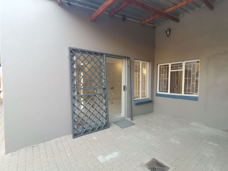 A covered patio area featuring paved flooring, timber rafters, and a secure metal gate entrance leading into the home.