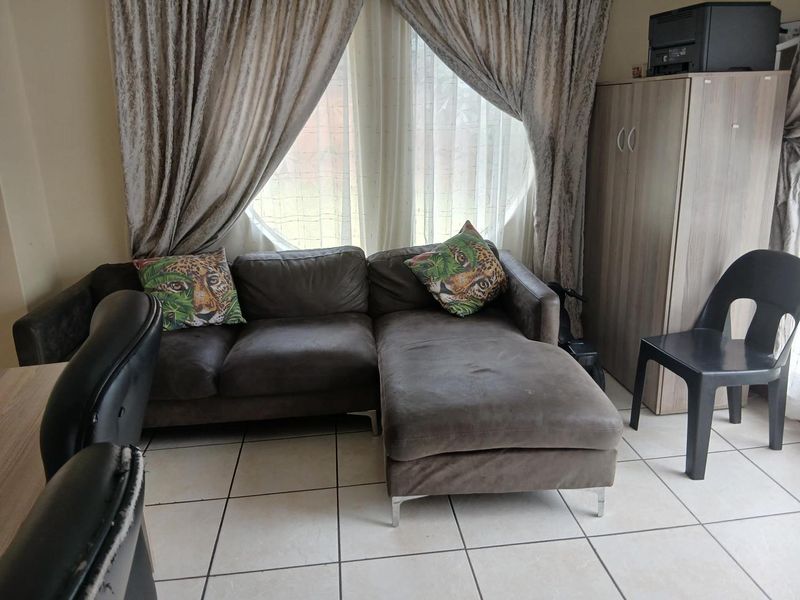 A living area featuring neutral ceramic floor tiles and a large window with curtains, providing natural light to the space.