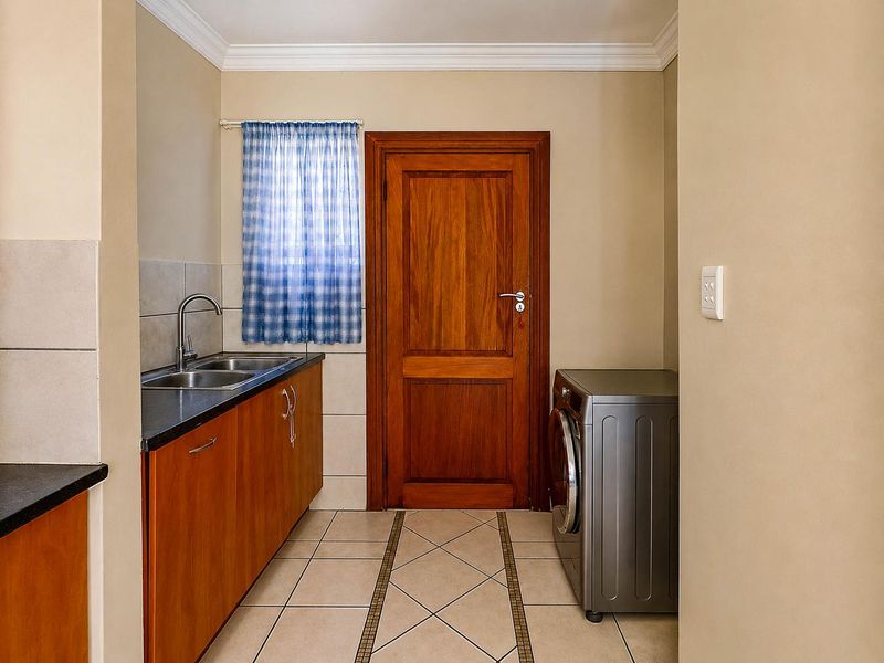 A functional laundry room featuring built-in cabinetry, a double sink, tiled flooring, and a solid wood door.