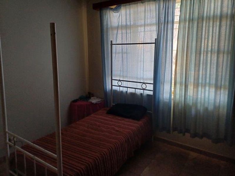 A bedroom featuring tiled flooring and a large window with curtains, providing natural light to the space.