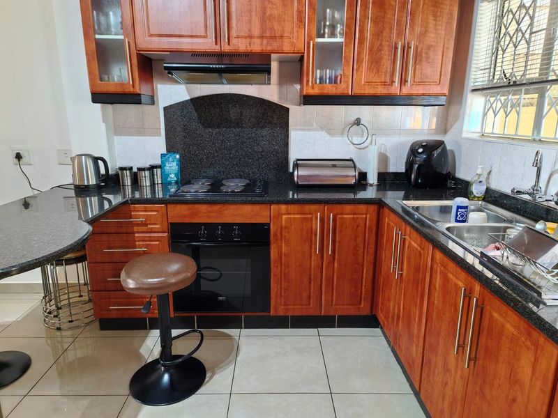 Functional kitchen featuring warm-toned wooden cabinetry, granite countertops, built-in oven, electric hob, and a double bowl sink with tiled flooring.