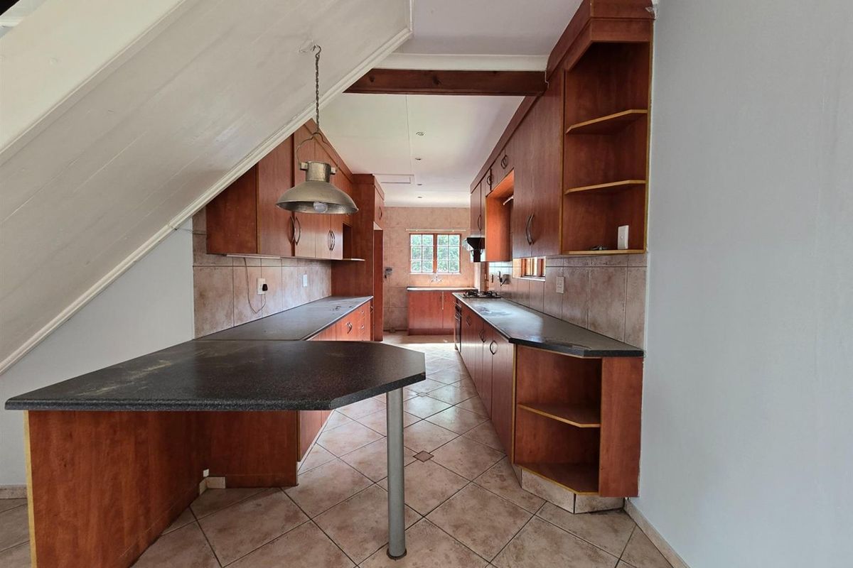 A galley-style kitchen featuring wooden cabinetry, dark laminate countertops, tiled flooring, and a built-in hob, situated beneath a staircase.