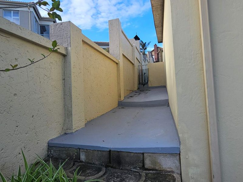 A narrow side passage featuring a concrete pathway and boundary wall, providing access along the side of the property.