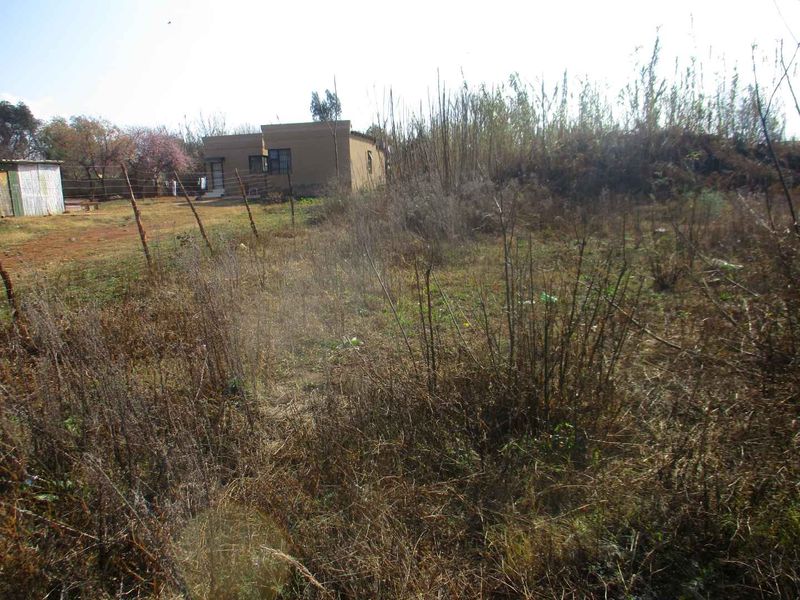 A view of the vacant residential land featuring overgrown vegetation, wire fencing, and a small outbuilding structure in the background.