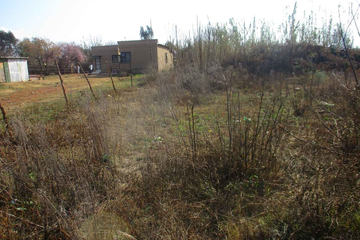 A view of the vacant residential land featuring overgrown vegetation, wire fencing, and a small outbuilding structure in the background.