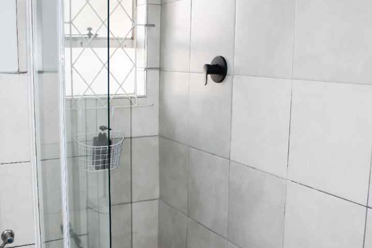 A clean, modern shower stall featuring neutral wall tiles, a mosaic-tiled floor, and a contemporary black shower fixture with a glass enclosure.