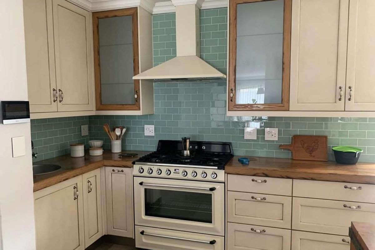 A well-appointed kitchen featuring cream cabinetry, a contrasting timber countertop, a gas range cooker with extractor hood, and a stylish teal subway tile backsplash.