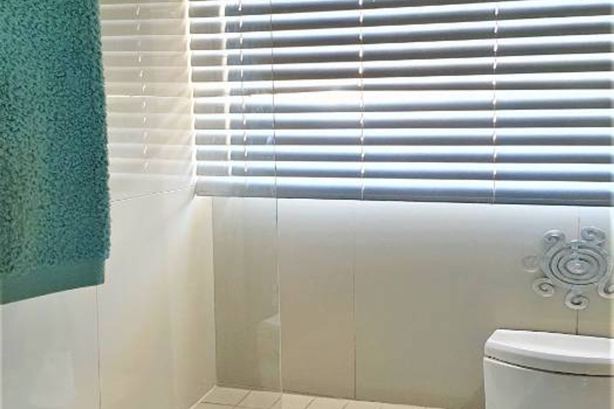 A functional bathroom featuring a bathtub with a glass shower screen, tiled walls, and a toilet, complemented by window blinds for privacy.