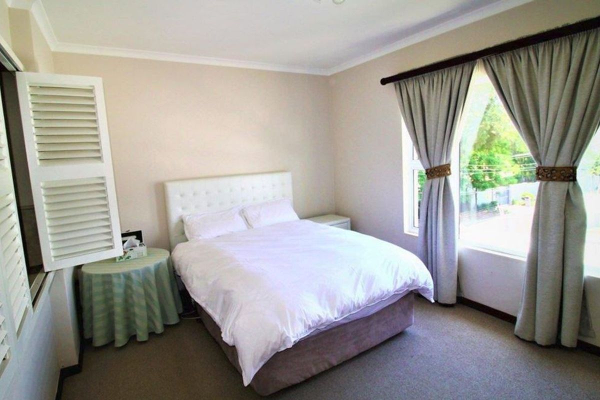 A well-maintained bedroom featuring neutral walls, carpeted flooring, built-in cupboards with plantation shutters, and a large window allowing for natural light.