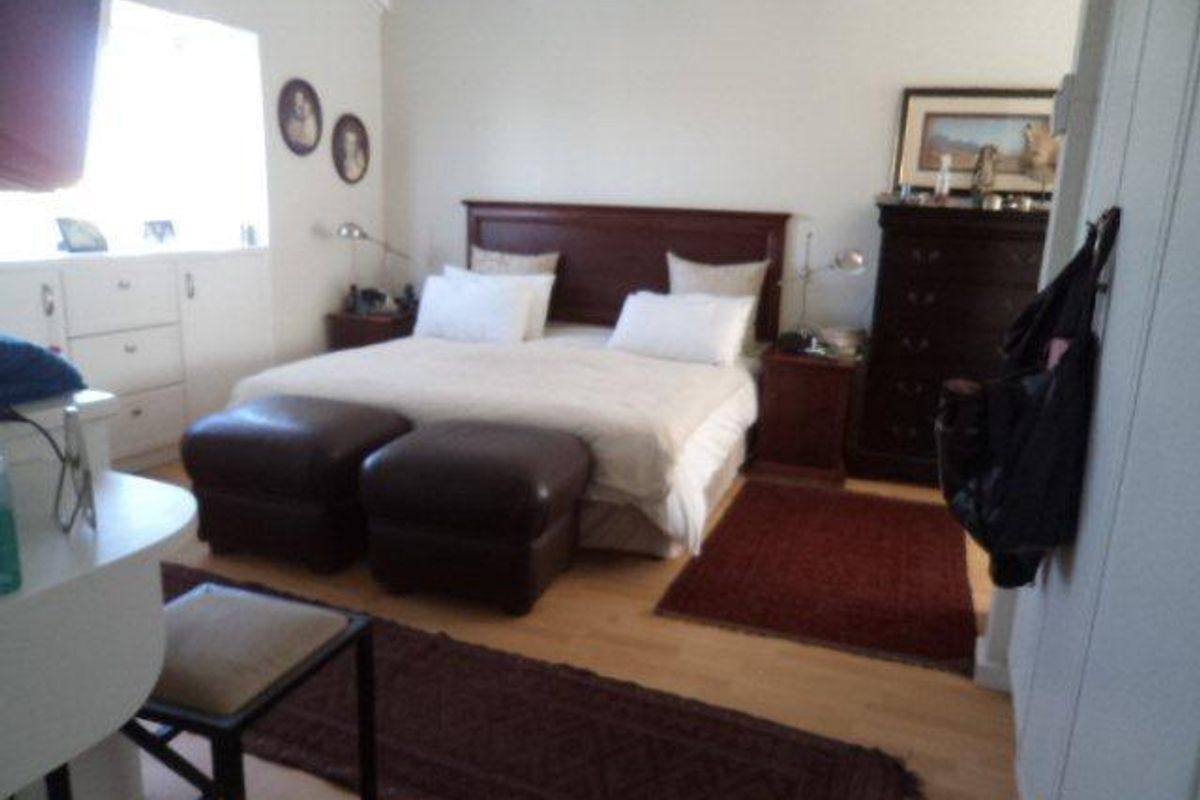 A spacious bedroom featuring light wood flooring, built-in cabinetry, and a vaulted ceiling with exposed beams.