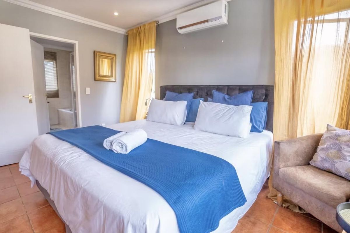 A well-maintained bedroom featuring tiled flooring, a wall-mounted air conditioning unit, and an en-suite bathroom access.