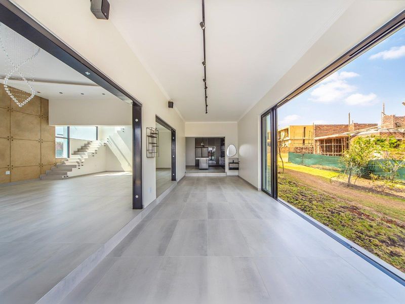 Spacious open-plan living area featuring large format floor tiles, modern track lighting, and expansive sliding glass doors opening to the garden.