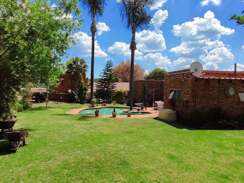 Spacious rear garden featuring a swimming pool and established lawn, set against a brick-built house exterior.