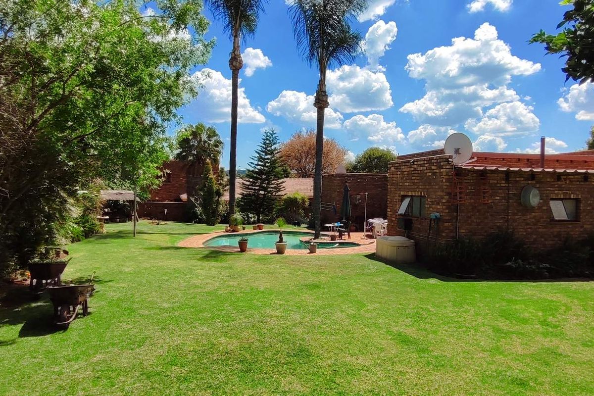 Spacious rear garden featuring a swimming pool and established lawn, set against a brick-built house exterior.