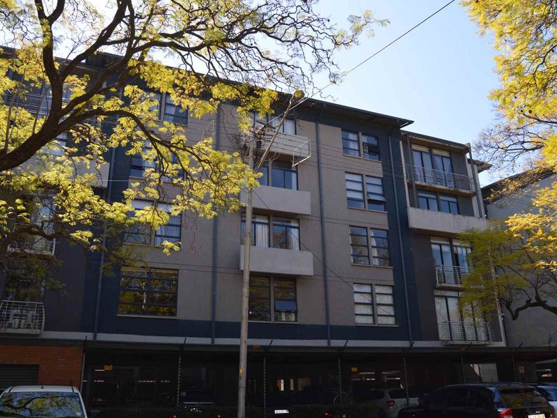 Exterior view of a multi-story apartment building featuring modern grey facade, private balconies, and a ground-level covered parking area.