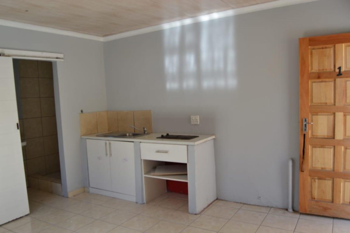 A compact kitchenette featuring basic cabinetry, a built-in hob, and a sink, set within a simple room with tiled floors and a timber ceiling.