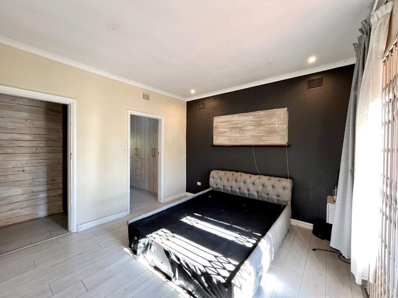 A bedroom featuring laminate flooring, recessed downlights, and built-in cupboards, with a neutral and dark accent wall design.