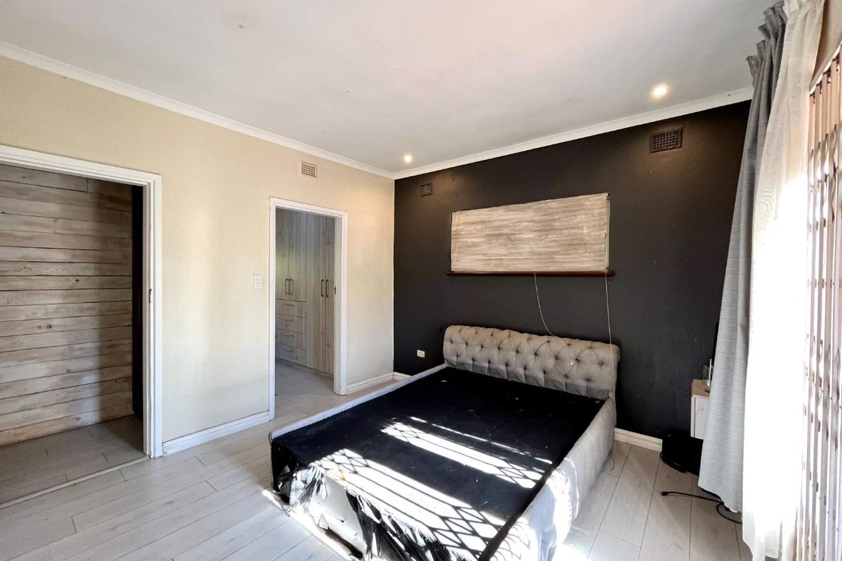 A bedroom featuring laminate flooring, recessed downlights, and built-in cupboards, with a neutral and dark accent wall design.