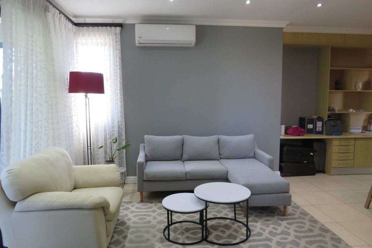 A comfortable living room featuring tiled flooring, recessed ceiling lighting, and a wall-mounted air conditioning unit.