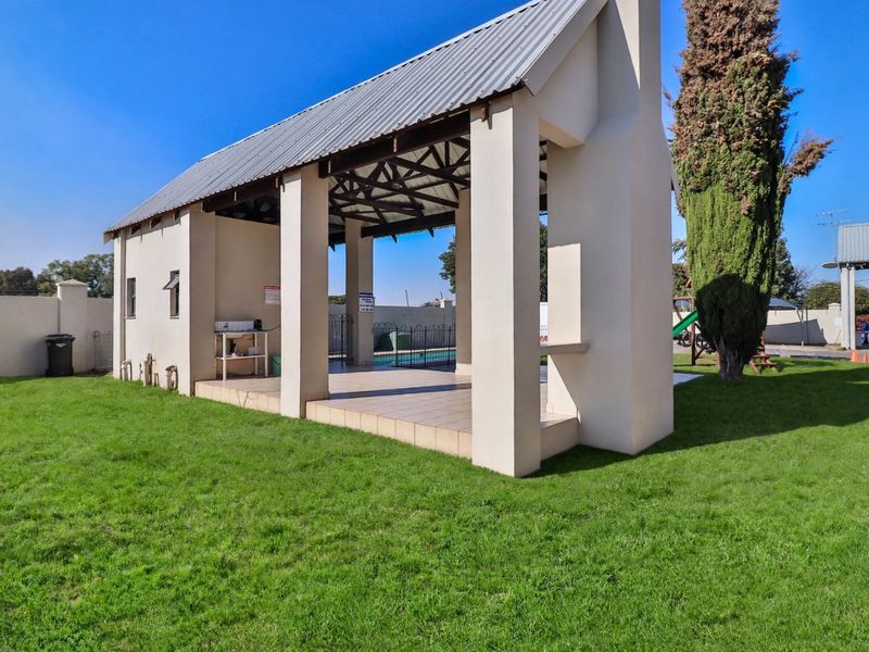 A spacious covered outdoor patio area featuring tiled flooring, masonry pillars, and a built-in fireplace chimney, set within a well-maintained garden.