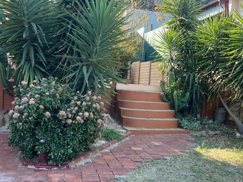 A landscaped garden area featuring brick paving, established plants, and concrete steps leading to a raised section of the property.