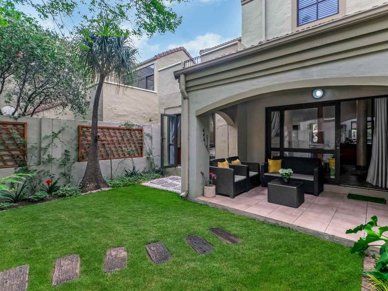 A well-maintained rear garden featuring a covered patio with tiled flooring, lush lawn, and established boundary walls with decorative trellis panels.