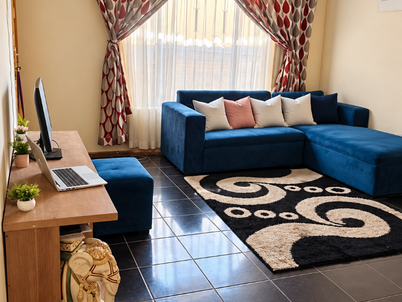 A living room featuring dark tiled flooring and large windows with patterned curtains, providing a functional and well-lit space.