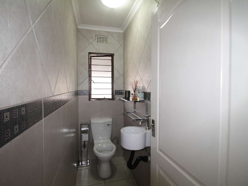 A compact guest bathroom featuring tiled walls, a wall-mounted basin, and a standard toilet with a security-grille window.