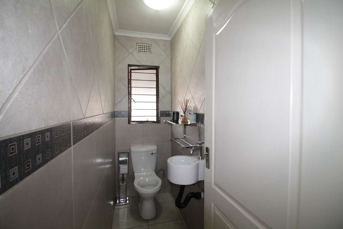A compact guest bathroom featuring tiled walls, a wall-mounted basin, and a standard toilet with a security-grille window.