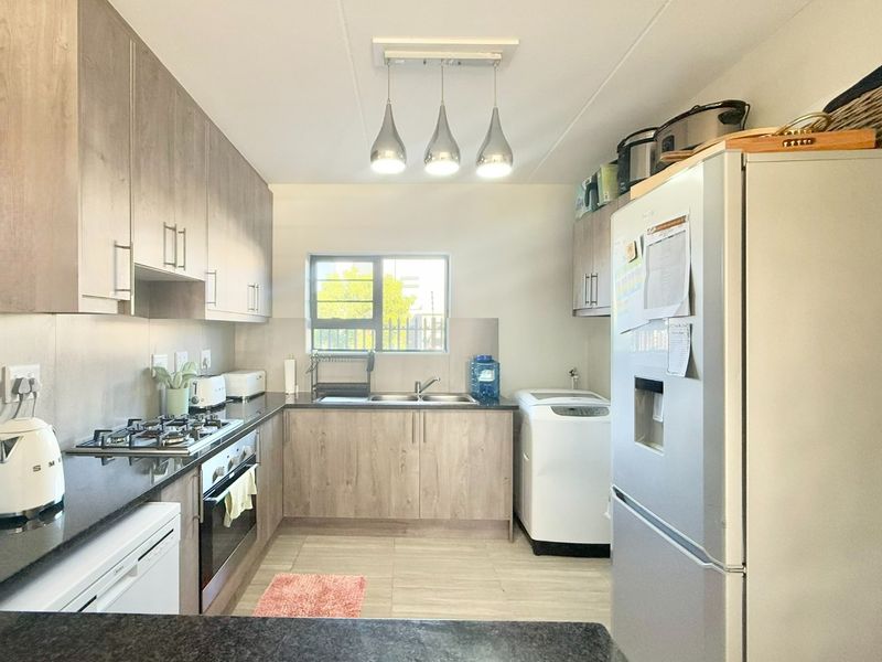 A well-maintained kitchen featuring modern wood-finish cabinetry, stone countertops, a gas hob, built-in oven, and integrated laundry plumbing.