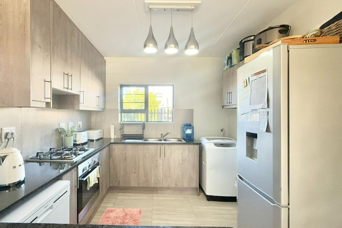 A well-maintained kitchen featuring modern wood-finish cabinetry, stone countertops, a gas hob, built-in oven, and integrated laundry plumbing.