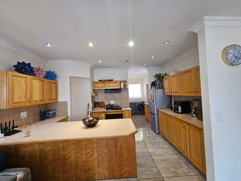Spacious kitchen featuring wooden cabinetry, laminate countertops, tiled flooring, and a functional layout with an integrated scullery area.
