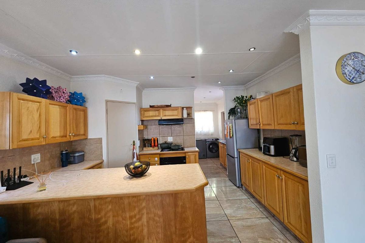Spacious kitchen featuring wooden cabinetry, laminate countertops, tiled flooring, and a functional layout with an integrated scullery area.
