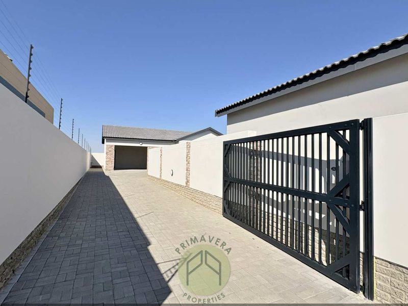 A clean, well-maintained paved driveway leading to a garage, featuring secure perimeter walls with electric fencing and a modern metal gate.