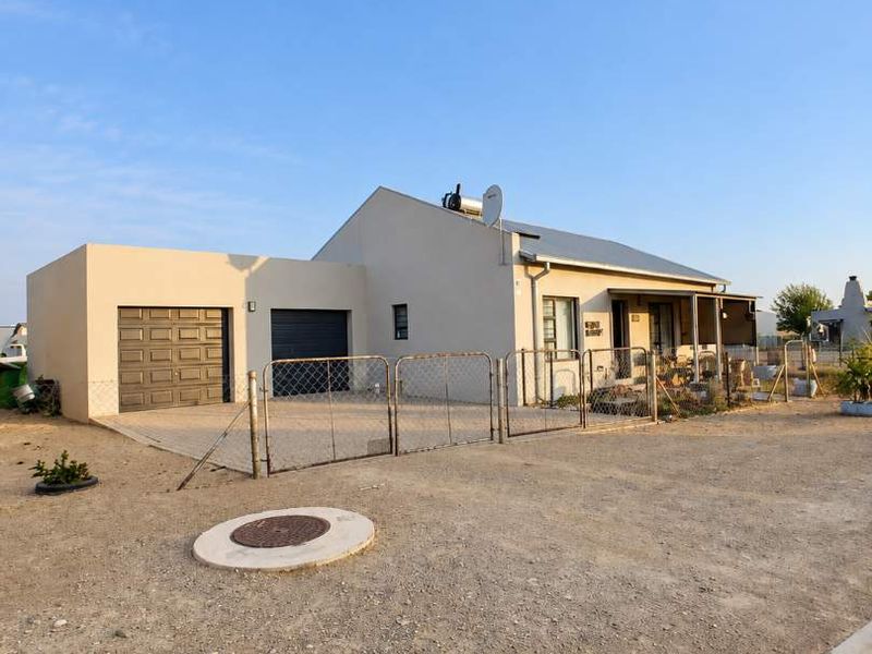 Front exterior view of a single-story house featuring a garage, metal roofing, solar water heater, and a gravel driveway with perimeter fencing.
