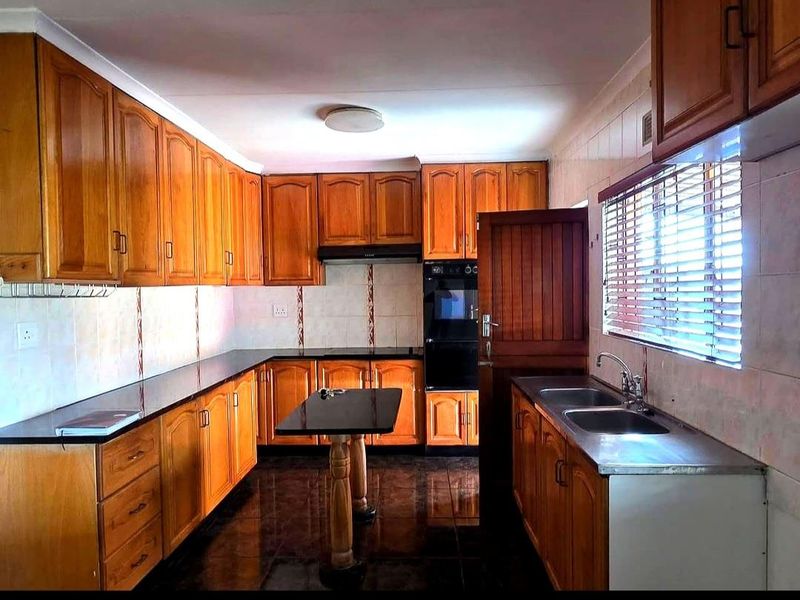 A functional kitchen featuring extensive wooden cabinetry, granite countertops, a double stainless steel sink, and built-in oven with extractor fan.