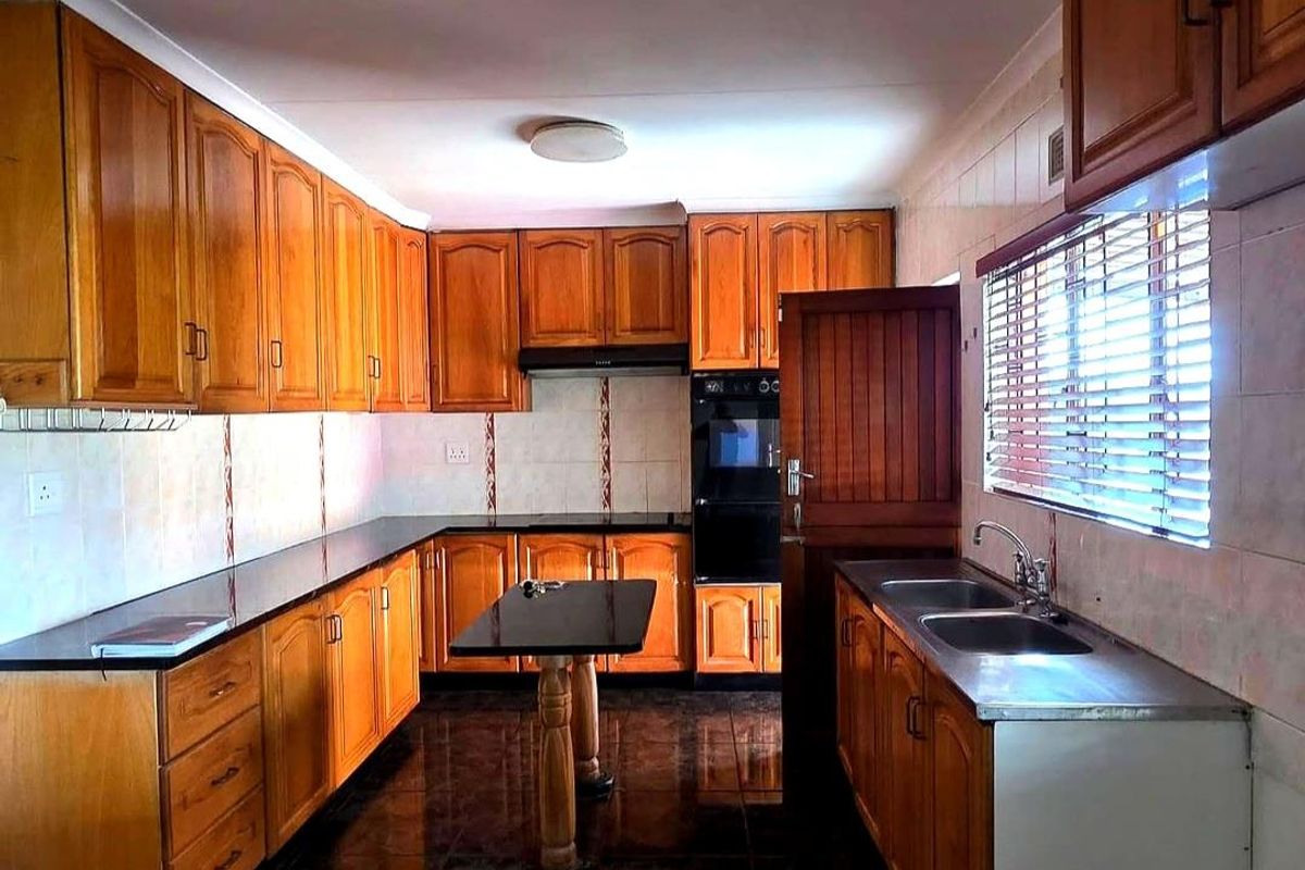 A functional kitchen featuring extensive wooden cabinetry, granite countertops, a double stainless steel sink, and built-in oven with extractor fan.