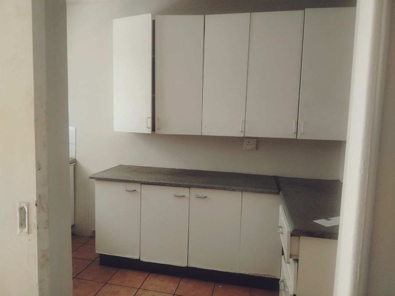 A compact, empty kitchen featuring white built-in cabinetry, laminate countertops, and tiled flooring, offering a blank canvas for potential renovation.