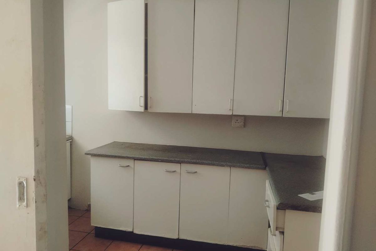 A compact, empty kitchen featuring white built-in cabinetry, laminate countertops, and tiled flooring, offering a blank canvas for potential renovation.