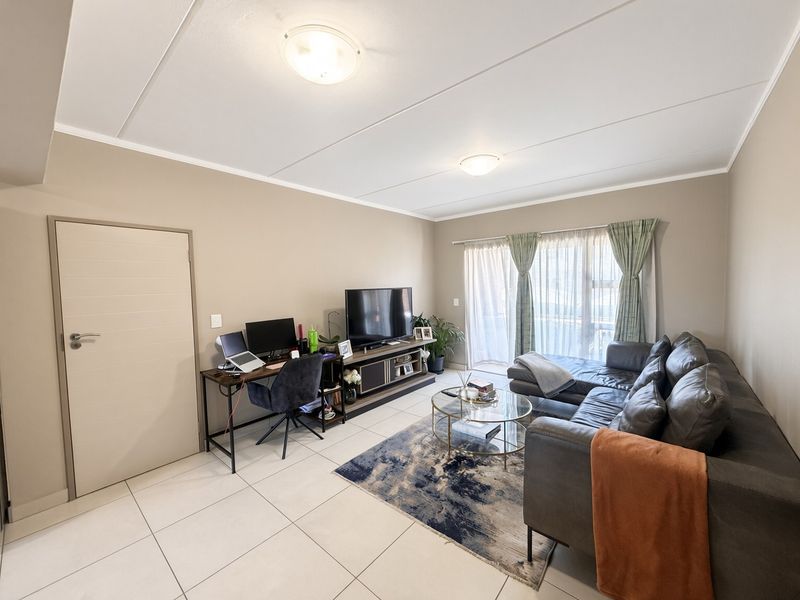 A well-maintained living room featuring neutral tiled flooring, flush mount lighting, and a sliding glass door providing access to the exterior.